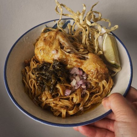 khao soi in a bowl with pickled vegetables shallot fried noodle lime chicken