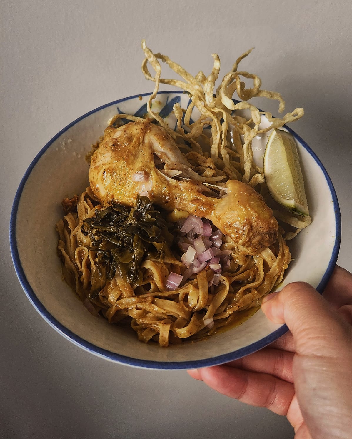 khao soi in a bowl with pickled vegetables shallot fried noodle lime chicken